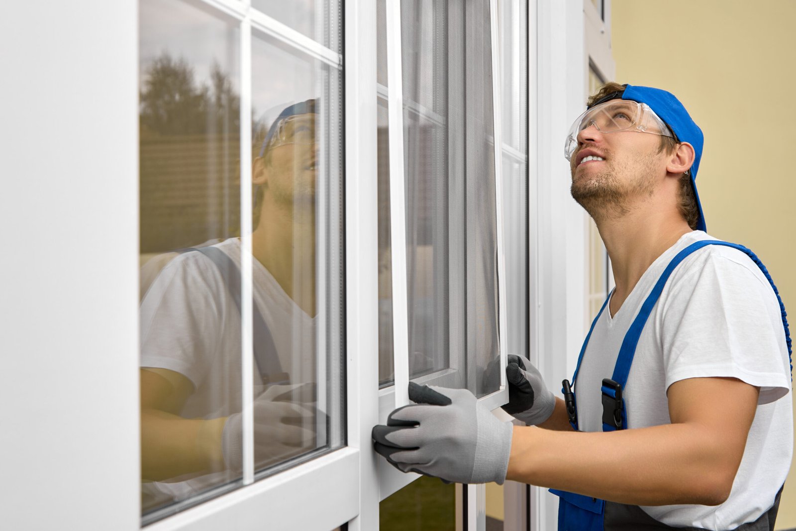 worker in overalls and goggles looks up with smile when installing mosquito net